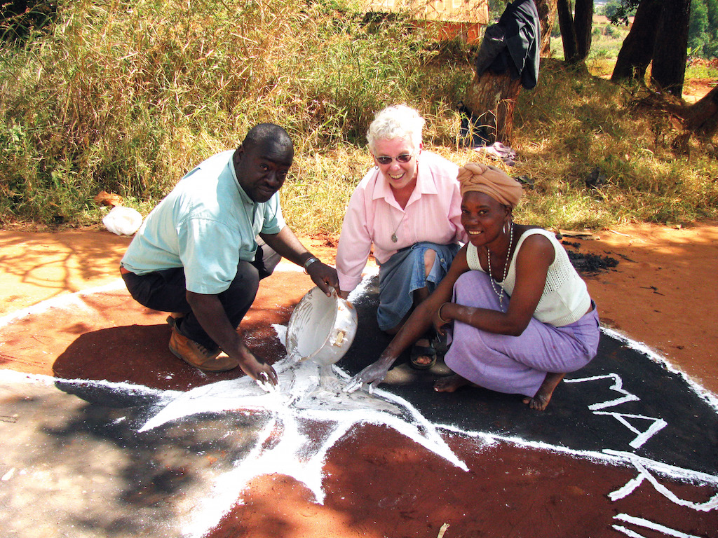 Scarboro missioner Sr. Ann MacDonald, and John and Trinitas, together with other members of the St. Maria Goretti faith community in Mzuzu, Malawi, use a paste to create circular symbolic houses and a path around the cathedral grounds. The bishop walked the path during the Feast of Corpus Christi in a symbolic gesture of carrying the Blessed Sacrament from house to house.