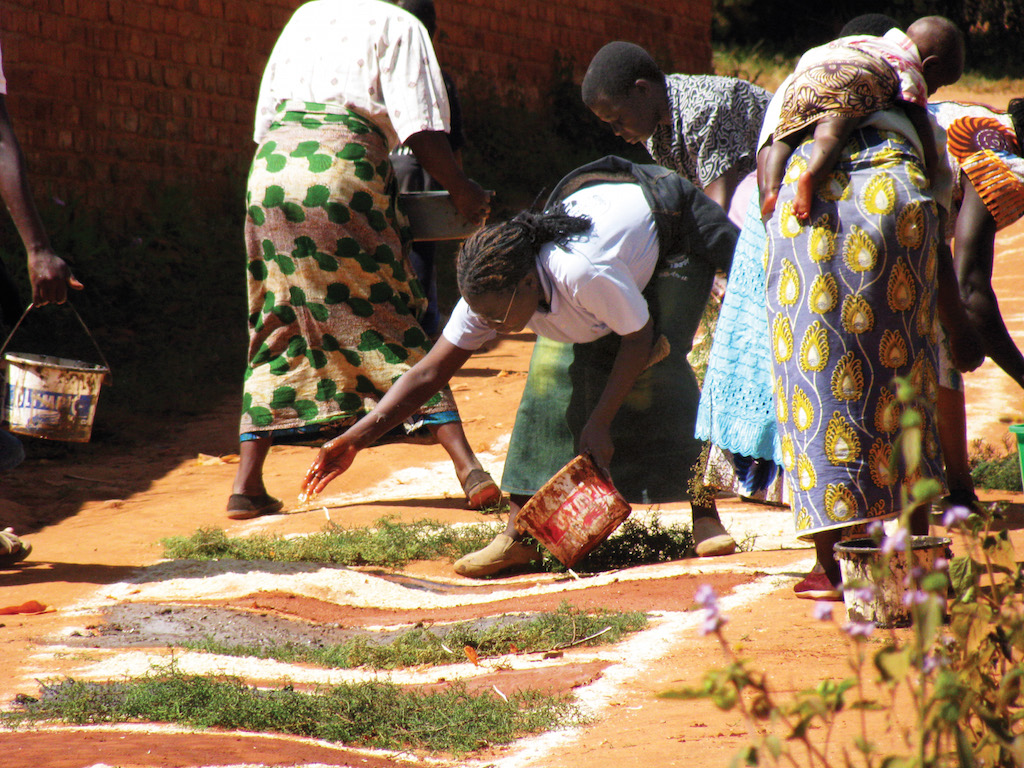 Scarboro missioner Sr. Ann MacDonald, and John and Trinitas, together with other members of the St. Maria Goretti faith community in Mzuzu, Malawi, use a paste to create circular symbolic houses and a path around the cathedral grounds. The bishop walked the path during the Feast of Corpus Christi in a symbolic gesture of carrying the Blessed Sacrament from house to house.