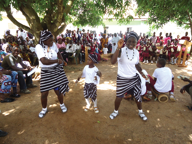 Students Senenge, Winnifred, and Mimidoo dancing for the guests. The school is located in Tivland and the black and white striped cloth worn by the dancers is the traditional cloth of the Tiv people.